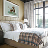 A primary bedroom in a hunting lodge with plaid bedding, there is a chocolate labrador retriever artwork above the bed